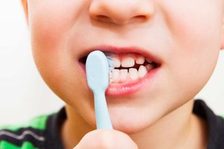 A child brushing their teeth with a children's toothbrush.